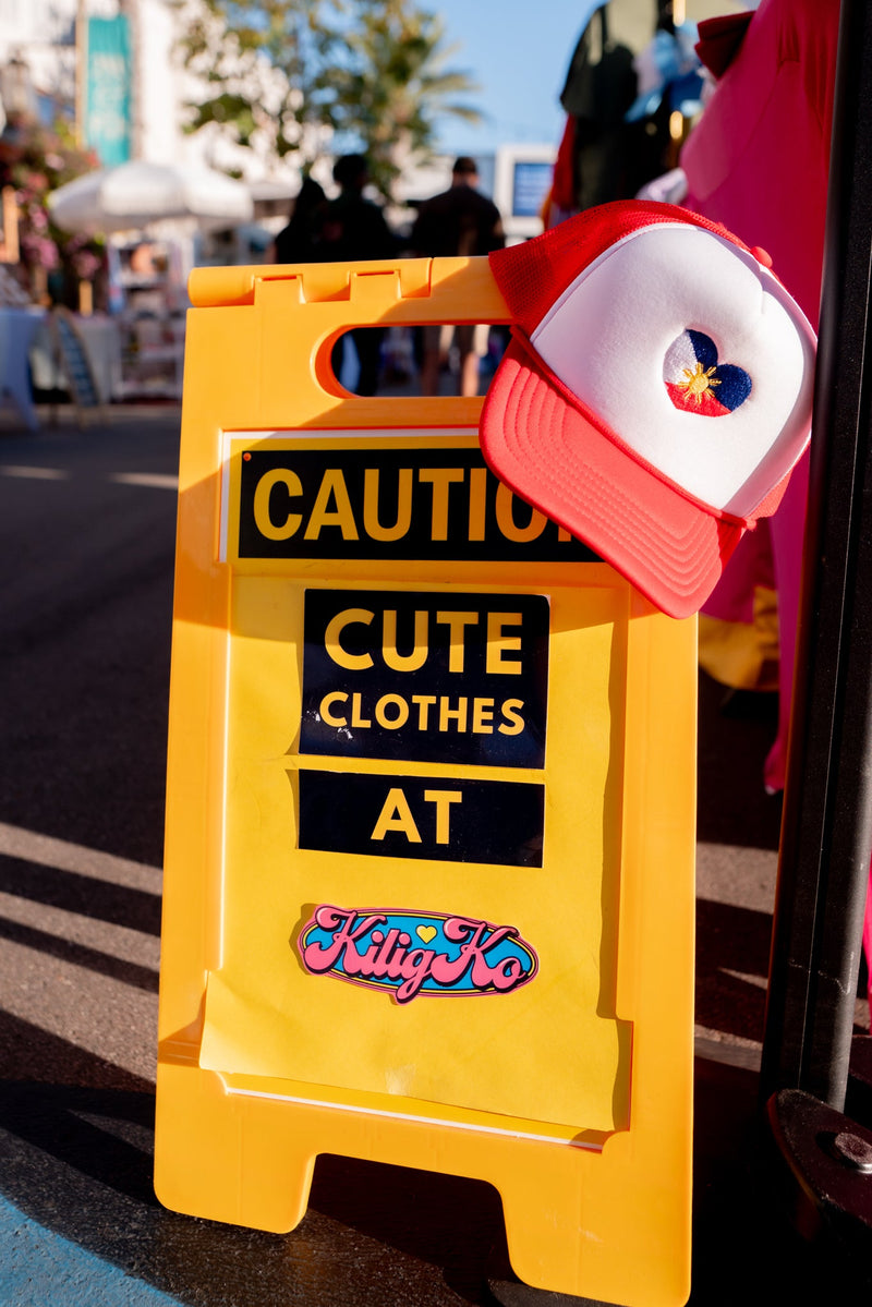 Kilig Ko event sign. Caution sine with text 'caution cute clothes at kilig ko' with a kilig ko cap hanging