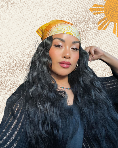Woman with long black hair wearing a yellow headscarf with a sun design on a textured beige background.