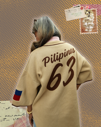 A person shown from behind wearing a beige oversized knit sweater with 'Pilipinas 63' printed in dark brown across the back. 